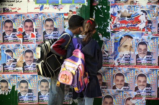 Egyptian students look Thursday at their school gate covered in election posters showing candidates for the coming parliamentary elections in Cairo. Rights activists in Egypt are struggling to ensure they will be able to monitor parliament elections Sunday that they expect to be plagued by rigging. But they are hoping for help from would-be voters themselves through an Internet map tracking violations at the polls.